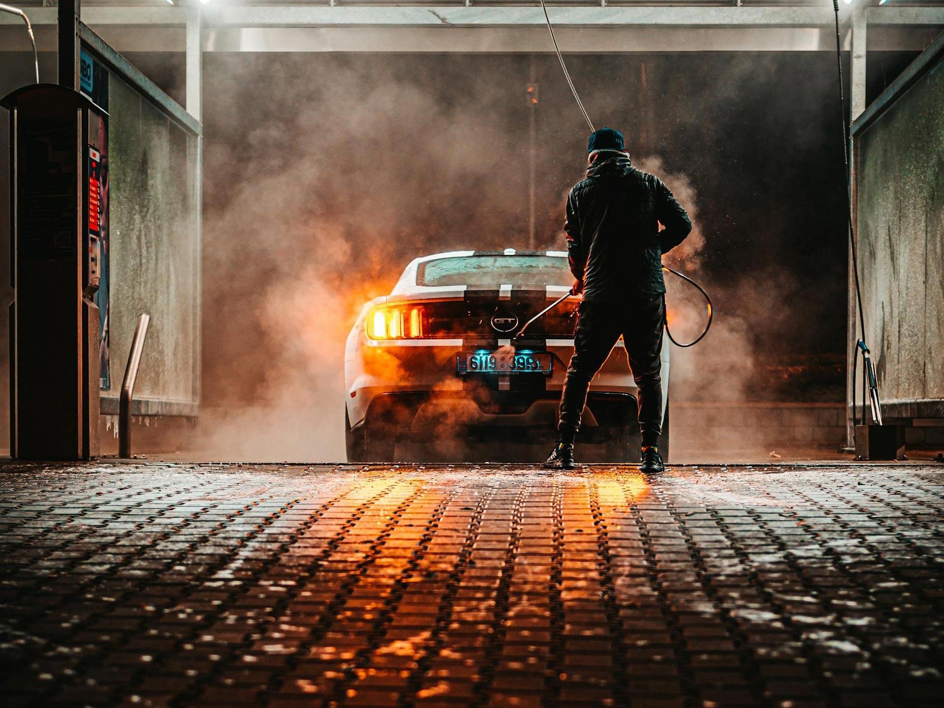 uomo di spalle lava auto scura con l'idropulitrice