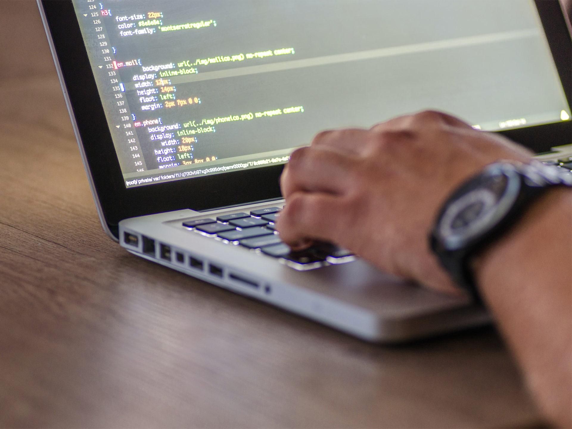 mano di uomo che digita sulla tastiera di un laptop con stringhe di codice sullo schermo