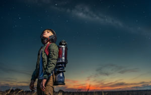 bambino con zaino che guarda il cielo al tramonto