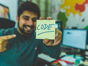 ragazzo sorridente tiene in mano e mostra un post it giallo con la scritta CODE