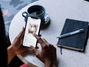 dito che scrolla feed di Instagram su un cellulare con tazza di caffè e agenda sullo sfondo