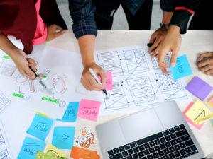 ragazzi disegnano wireframes su fogli di carta sopra una scrivania