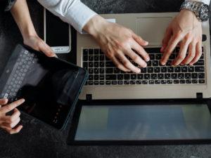 mani che digitano sulla tastiera di un laptop e mani che reggono un tablet
