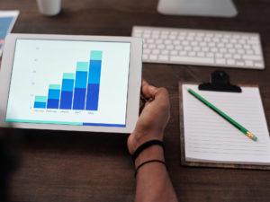 tablet con grafico in crescita sopra una scrivania con blocco di appunti e pc