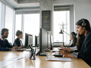 persone con cuffie alle orecchie sedute a un tavolo davanti a pc
