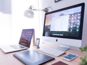 laptop, pc, tavoletta grafica e smartphone su una scrivania di legno ben illuminata
