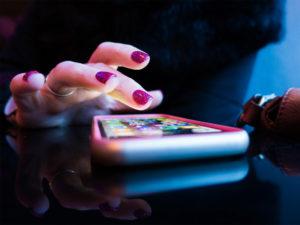 mano di donna che fa tap su smartphone su sfondo scuro