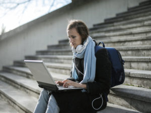 ragazza seduta su scalinata all'aperto con laptop sulle ginocchia