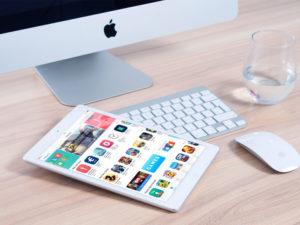 tablet con app sullo schermo, mouse e pc su scrivania in legno chiaro