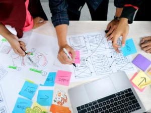 persone lavorano a bozze di UI/UX design sopra un tavolo bianco con laptop