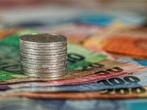 Banconote di vari tagli di euro e pila di monete da 2 euro appoggiate su un piano
